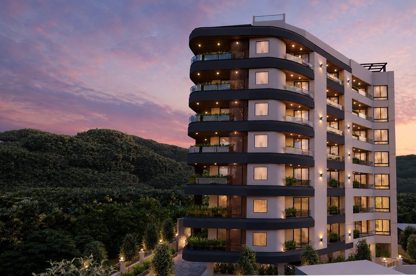 Curved residential apartment block at dusk against a wooded hillside.